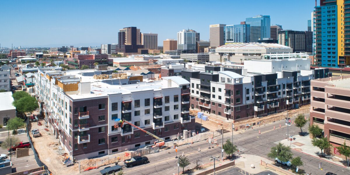 Aerial view of a cityscape featuring multi-story buildings under construction, parking lots, and high-rise structures in the background on a clear day.
