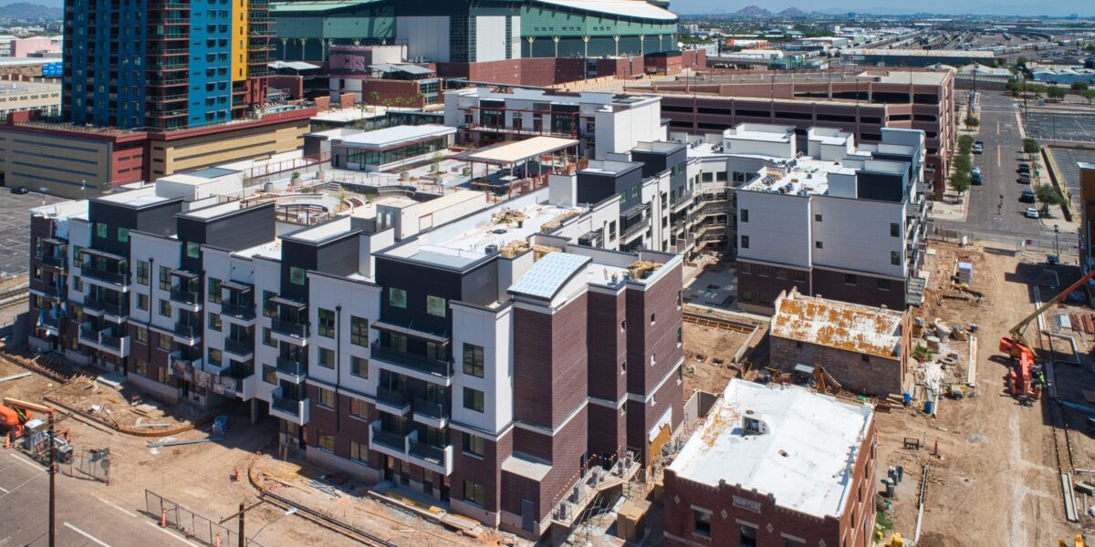 Aerial view of a construction site with new apartment buildings in progress, near a large stadium and high-rise in an urban area.