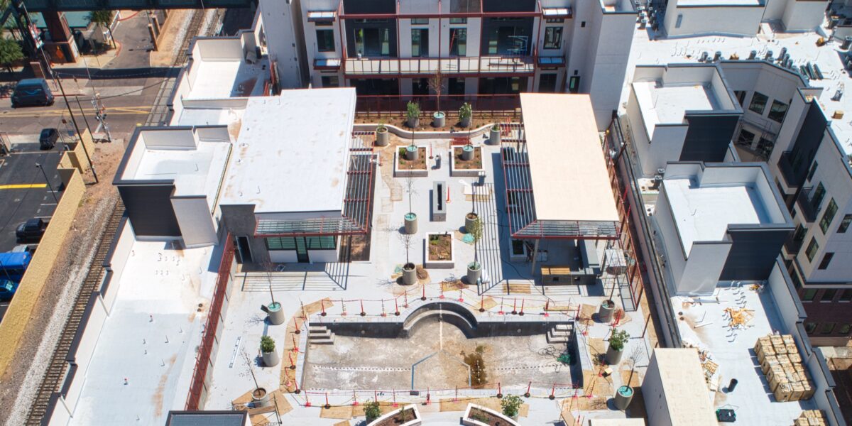 Aerial view of a modern, unfinished rooftop courtyard with walkways, planters, seating areas, and construction materials scattered around.